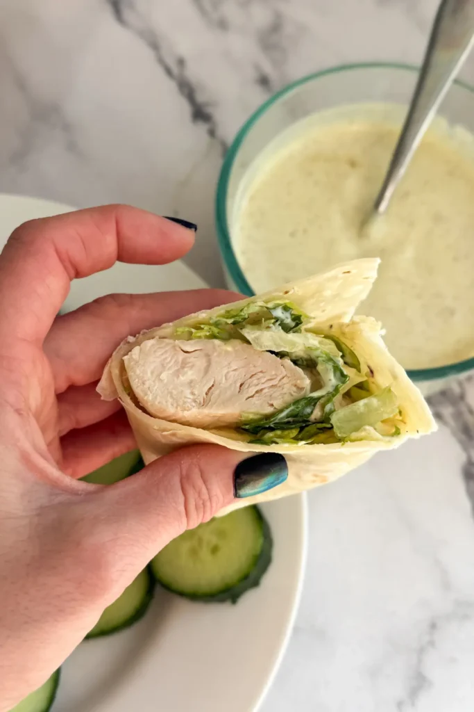 Someone holding a chicken honey mustard wrap in between their hands with a bowl of honey mustard in the background.