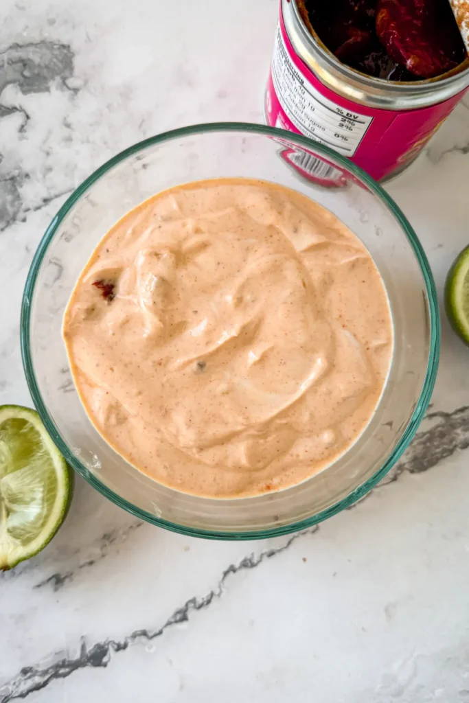 A smoky chipotle adobo Greek yogurt sauce in a glass bowl next to a can of adobo chipotle peppers on a counter.