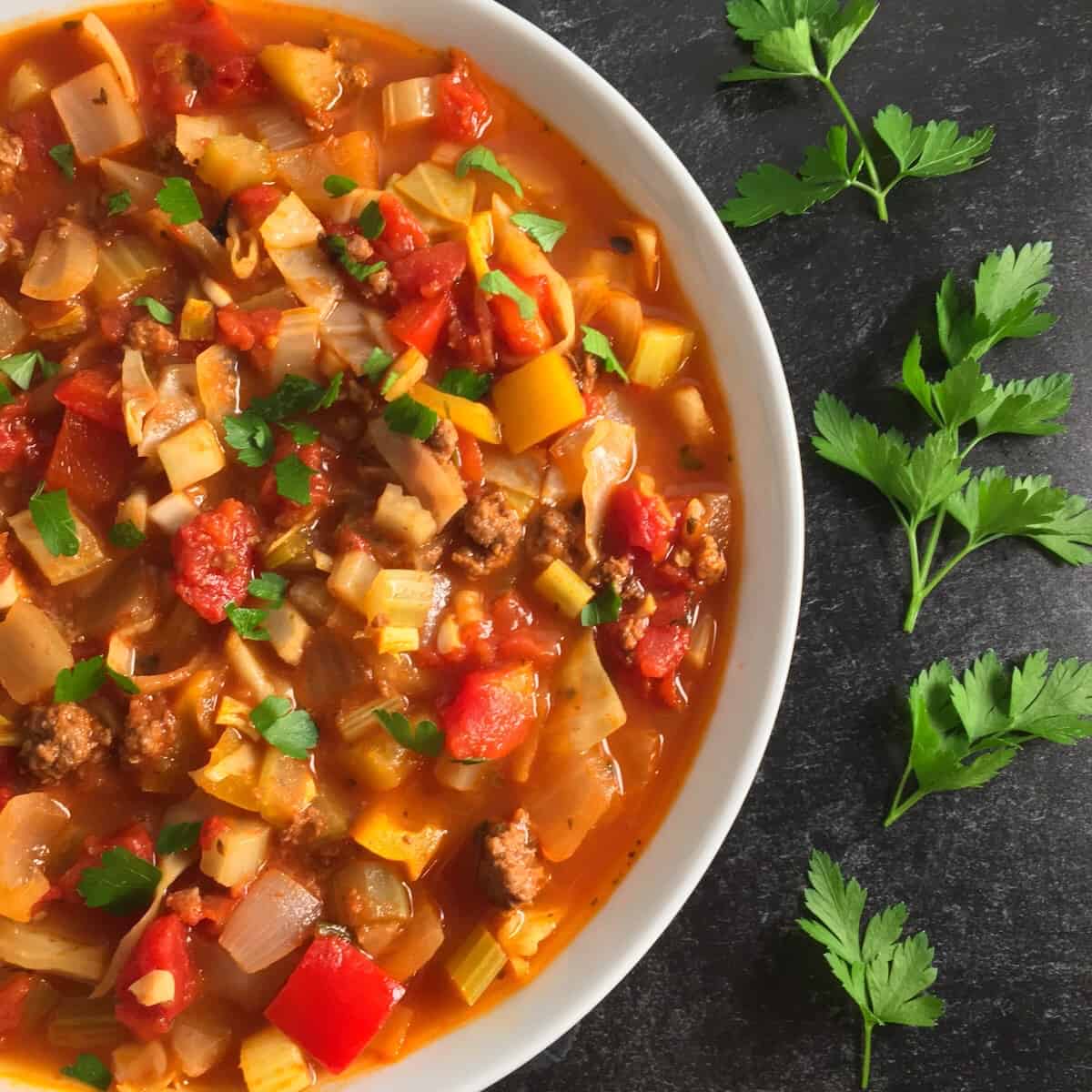 A close-up of a bowl of cabbage soup with veggies and lean ground beef. 