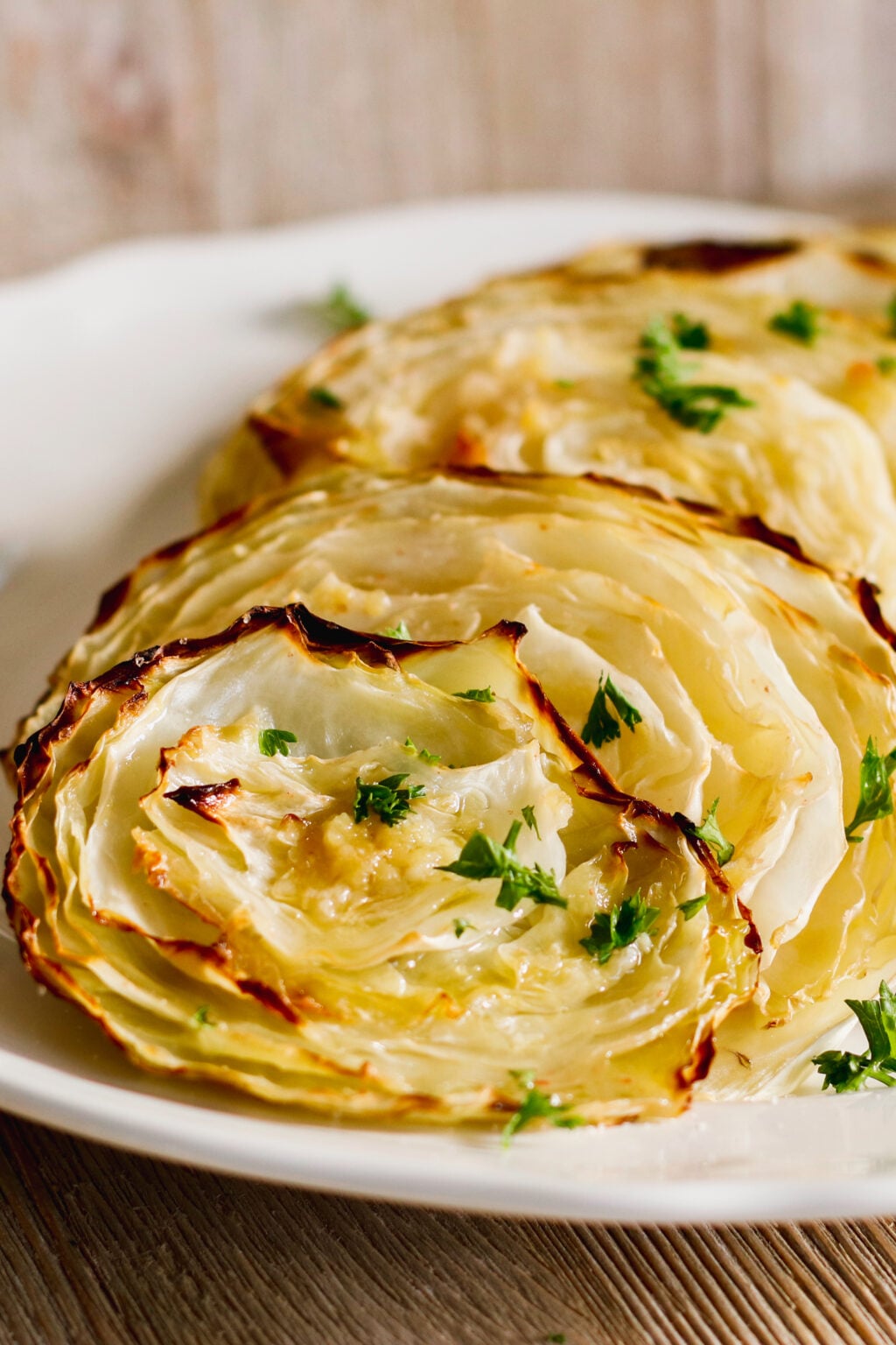 Two cabbage steaks on a white plate.