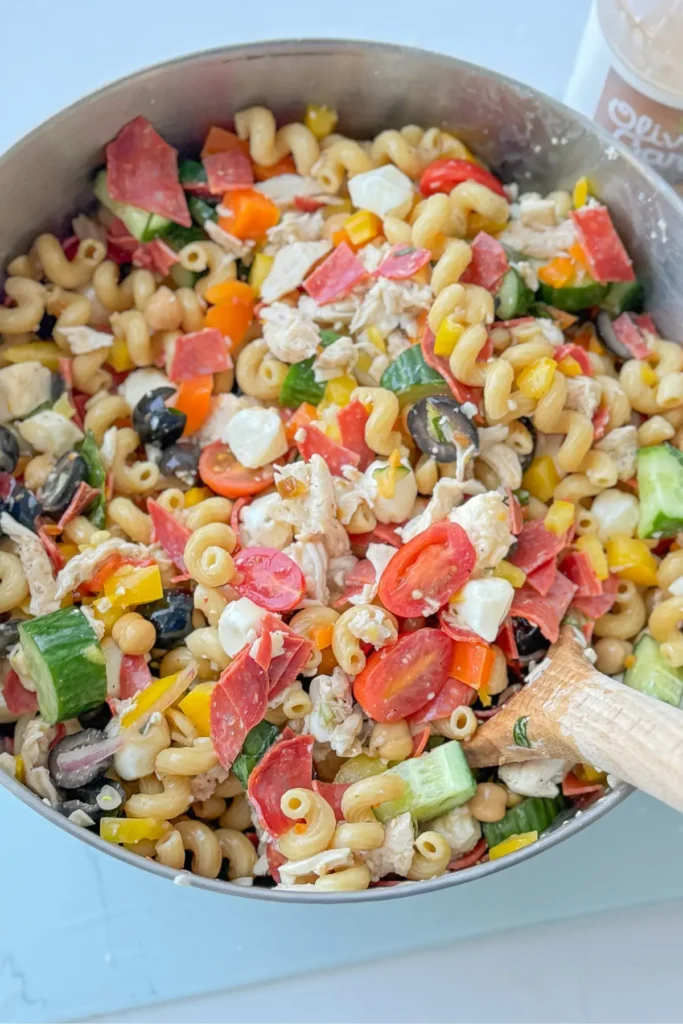 A large bowl of caprese pasta salad with a wooden spoon in it on a counter.