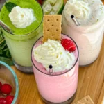 A birds-eye view of three delicious and healthy smoothies: a green refresher, a raspberry key lime pie and a strawberry basil on a wooden cutting board.