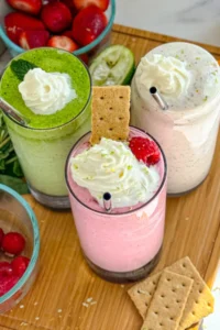 A birds-eye view of three delicious and healthy smoothies: a green refresher, a raspberry key lime pie and a strawberry basil on a wooden cutting board.