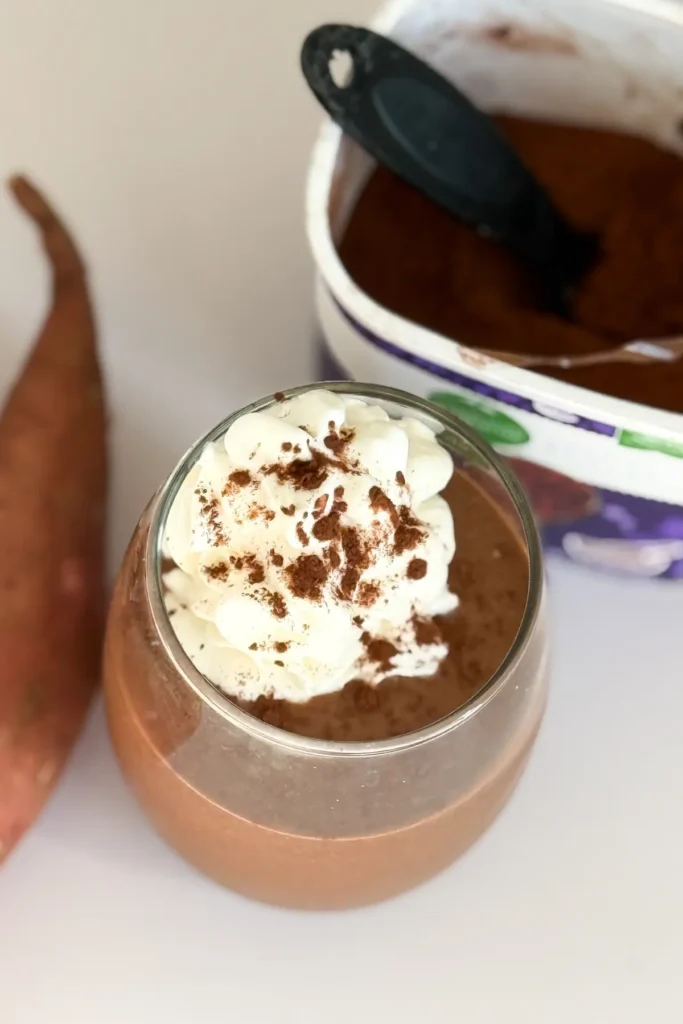 A birds-eye view of a chocolate sweet potato smoothie next to a carton of cacao powder.