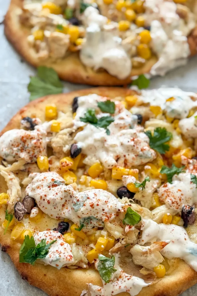 A close-up of two street corn chicken flatbreads topped with a cilantro and yogurt drizzle on a baking sheet.