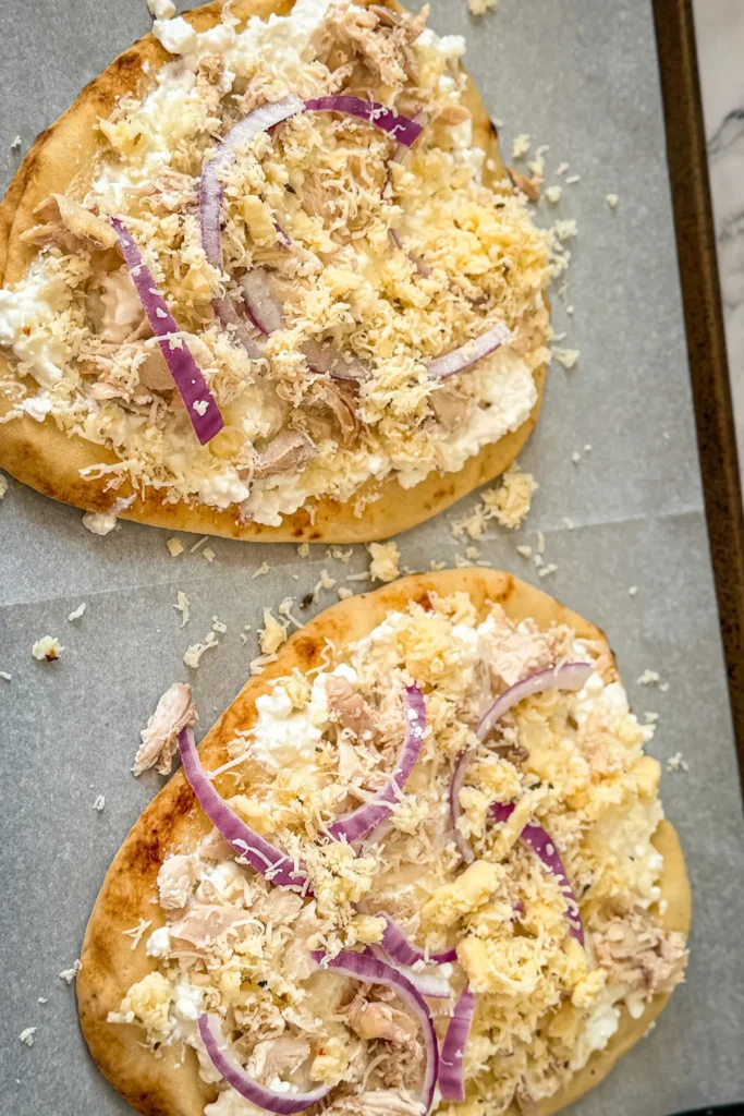 Cottage cheese spread on flatbreads with chicken, cheese and red onion on a baking sheet prior to baking.