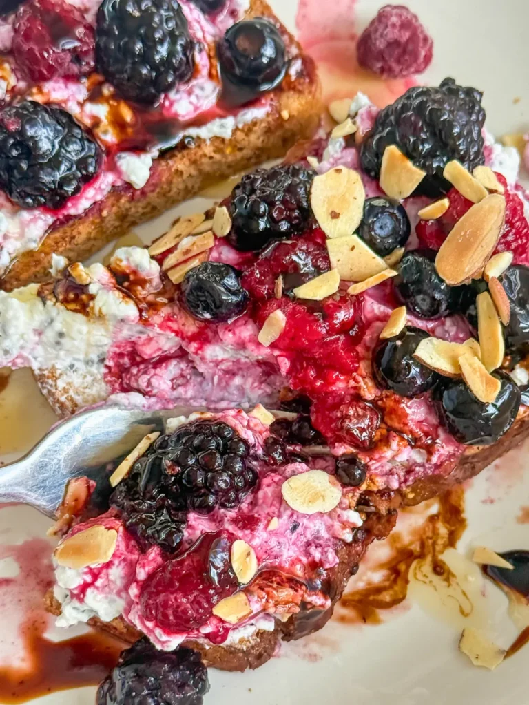 A fork digging into cottage cheese breakfast toast topped with slivered almonds and berries.