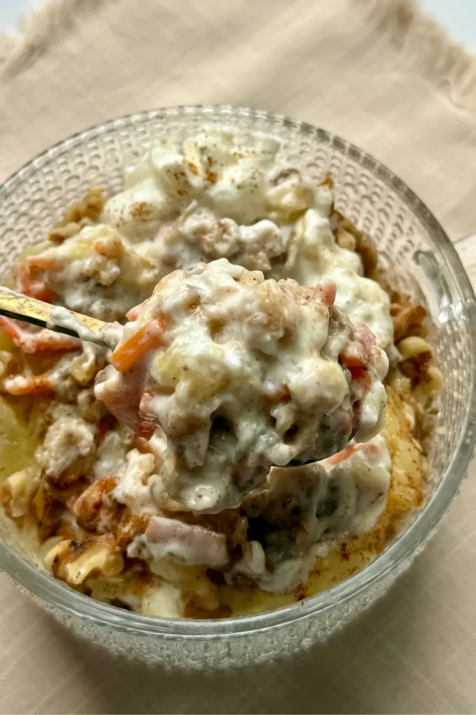 A spoon digging into a loaded oatmeal bowl mixed with a Greek yogurt protein powder frosting on a beige napkin on a table.