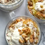 A birds-eye view of three loaded carrot cake oatmeal bowls topped with Greek yogurt cream cheese frosting, chopped walnuts and crushed pineapple on a table.