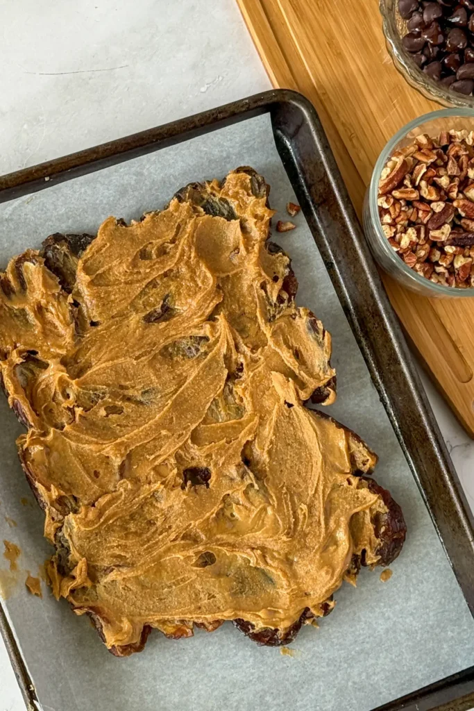 Dates spread out on a baking sheet lined with parchment paper topped with nut butter.