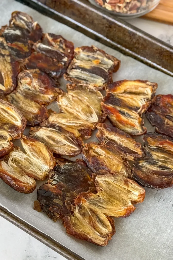 15 dates opened and spread out on a piece of parchment paper on a baking sheet.