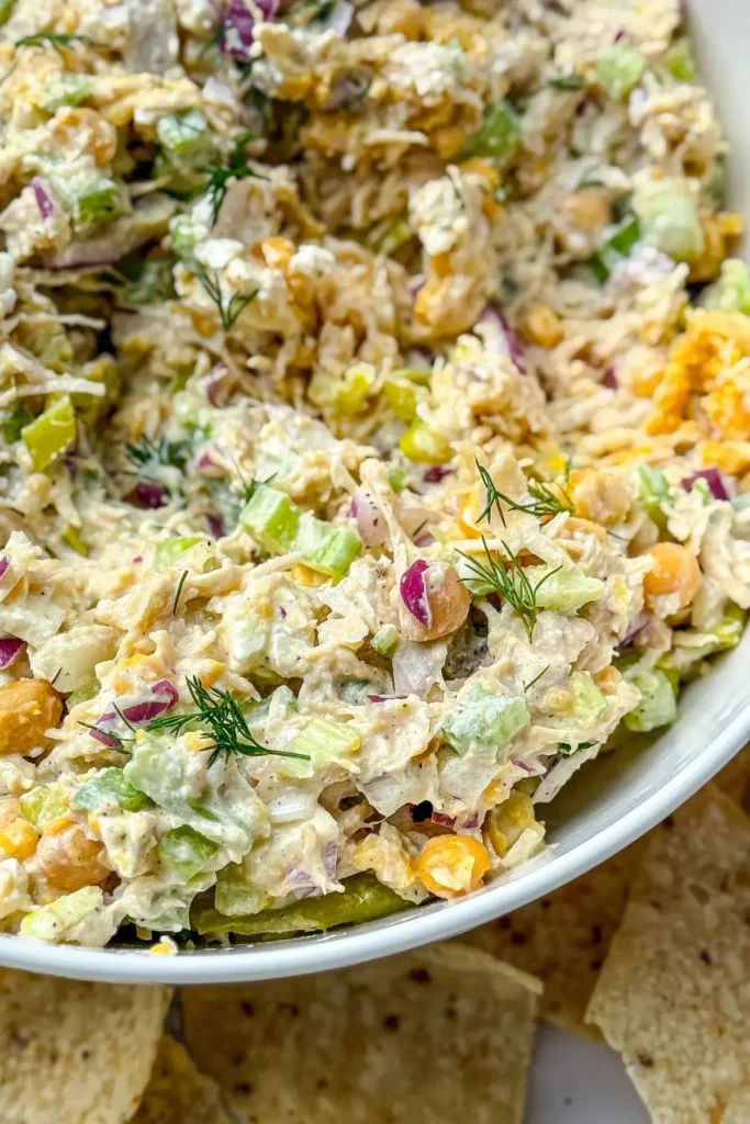A close-up birds-eye view of a large white bowl of chicken salad surrounded by tortilla chips. 