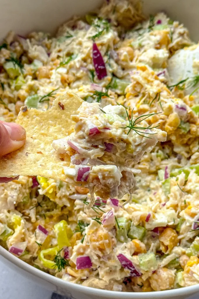 A birds-eye view of a chip with chicken salad on it over a large bowl. 