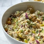 A large white bowl full of pepperoncini chicken salad on a counter next to a bowl of chips.