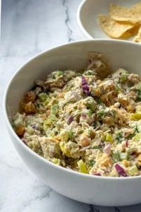 A large white bowl full of pepperoncini chicken salad on a counter next to a bowl of chips.