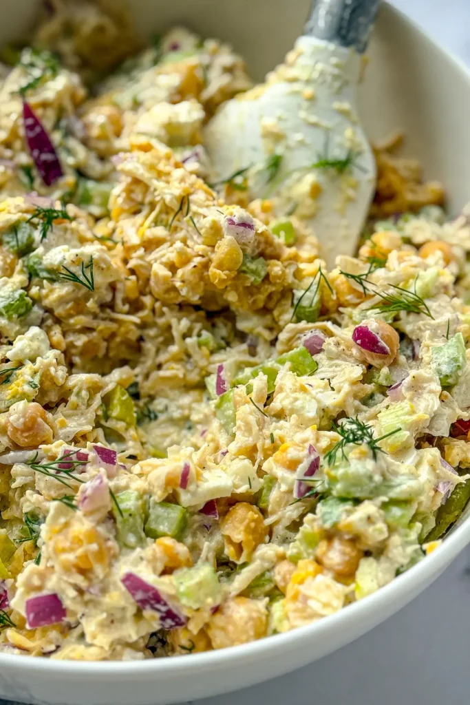 A close-up of the chicken salad in a white bowl after mixing with a spatula in it.