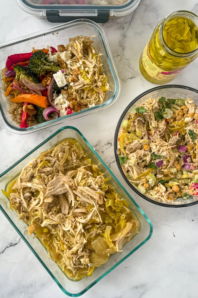 A birds-eye view of the leftover shredded chicken, the chicken salad, and a meal prep bowl on a counter in storage containers.