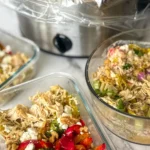 A slow cooker with shredded pepperoncini chicken in it next to a storage contaner of a chicken and quinoa bowl and a big container of chicken salad on a counter.