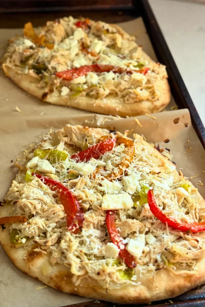 Two pepperoncini naan flatbreads with peppers and feta on a baking sheet lined with parchment paper. 