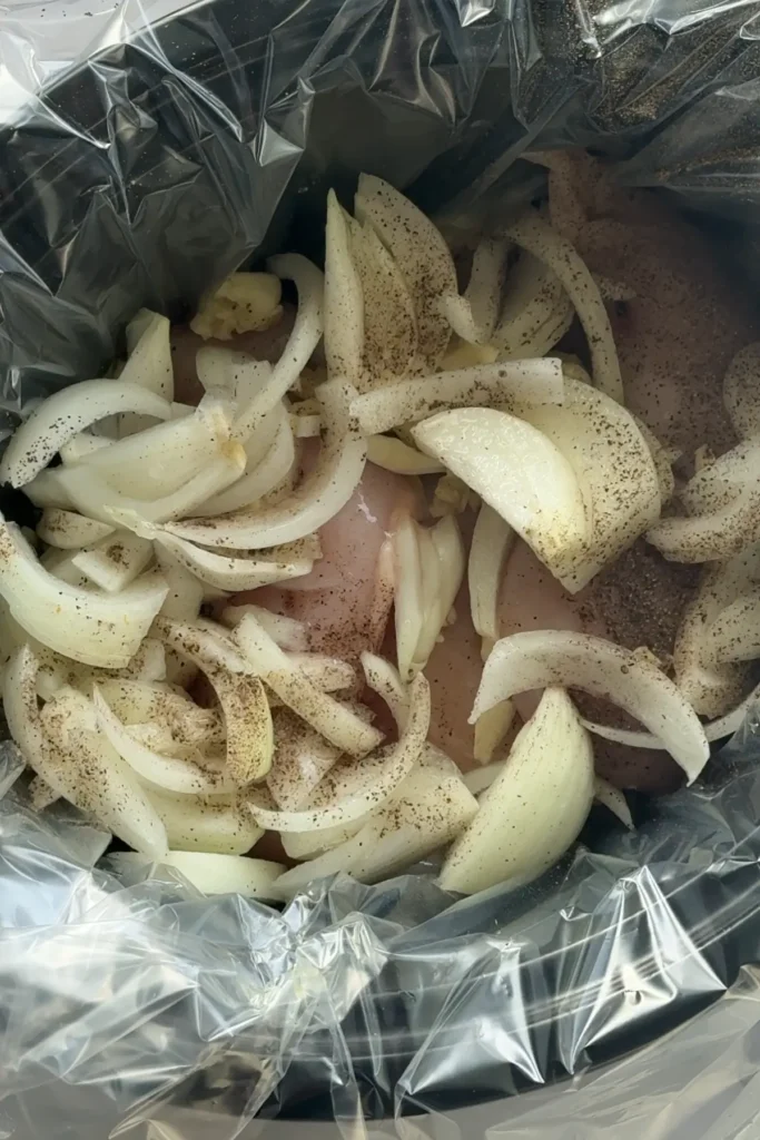 Raw chicken breast and onions in a slow cooker.