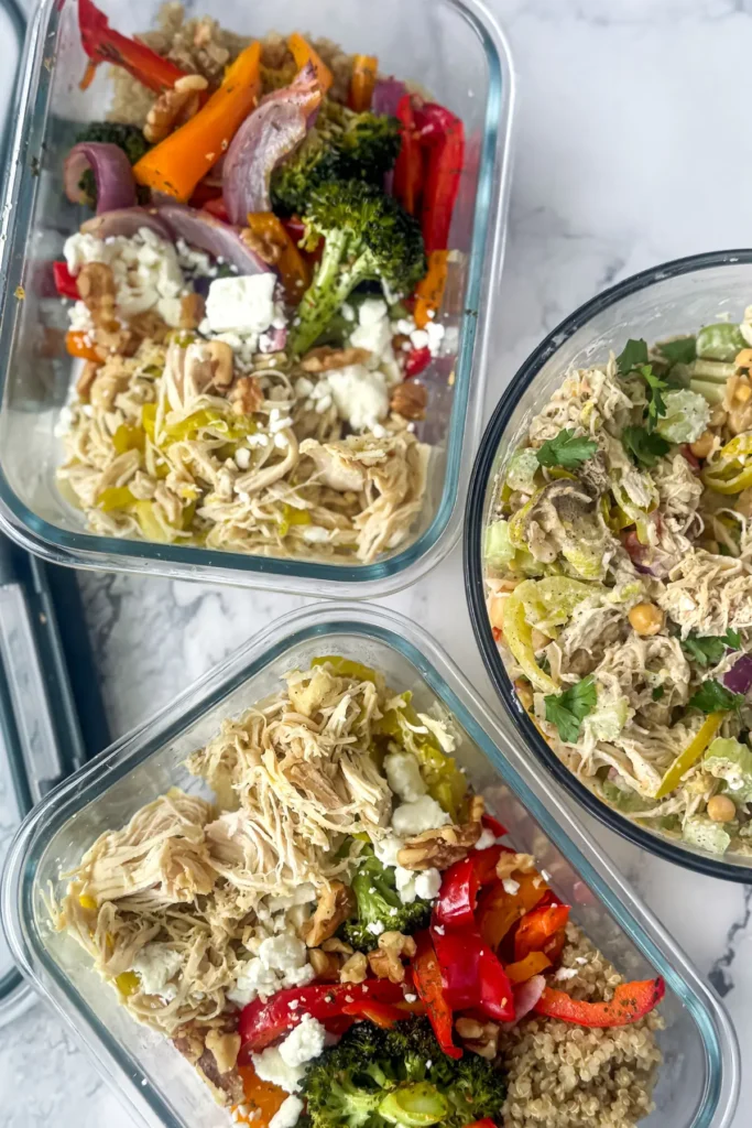 Two roasted veggie and quinoa meal prep bowls next to chicken salad on a counter.