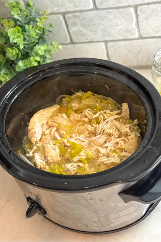 The pepperoncini chicken cooking in a slow cooker on a counter without the top on. 