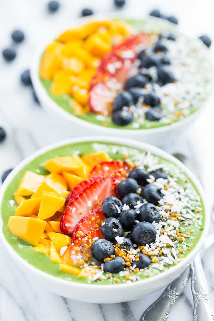 Two green smoothie breakfast bowls topped with fruit on a table.