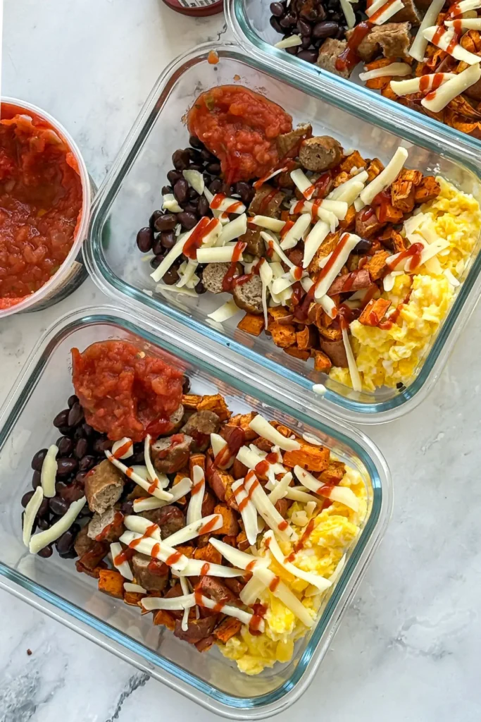 A birds-eye view of three glass containers with sweet potatoes, black beans, eggs, turkey sausage and cheese next to salsa.