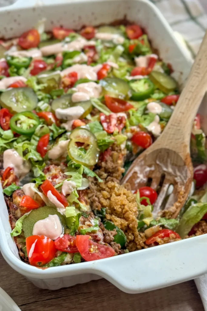 A wooden spoon digging into a cheeseburger casserole with hidden lentils in a white baking dish on a counter.