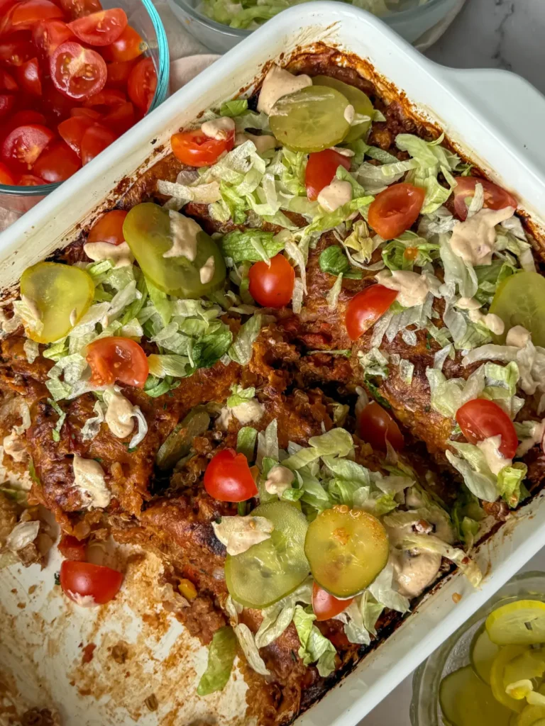 A birds-eye view of a cheeseburger lentil casserole cut into four pieces on a counter next to a bowl of tomatoes.