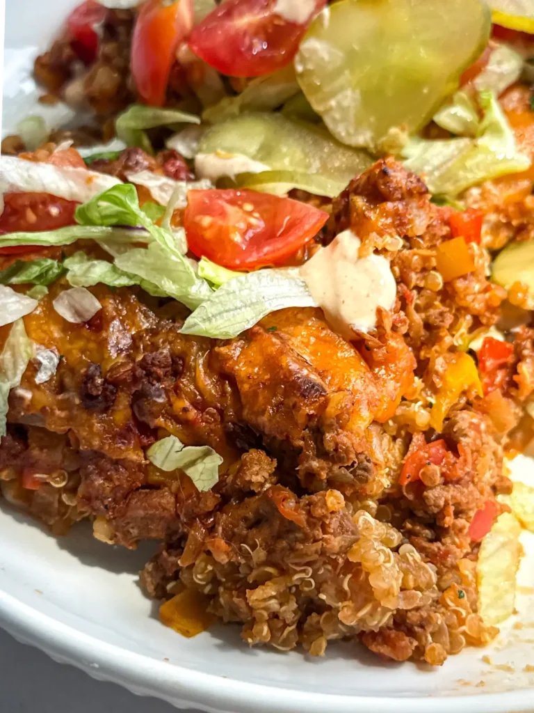 A cheeseburger casserole slice on a white plate, topped with shredded lettuce, special sauce, lettuce and tomatoes.