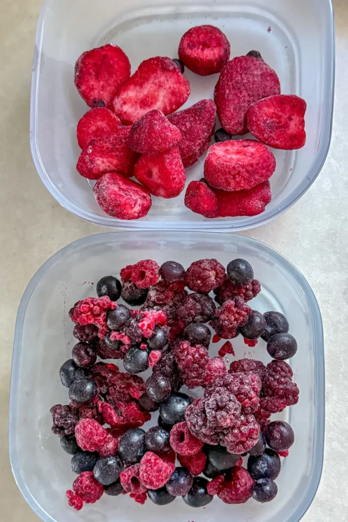 Two meal prep containers with frozen fruit and chia seeds in them on a counter.