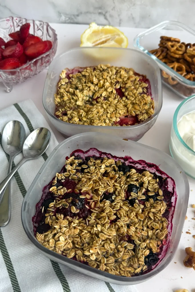 Two fruit cobblers right out of the oven on a counter next to a bowl of yogurt, pretzels, and a bowl of strawberries.