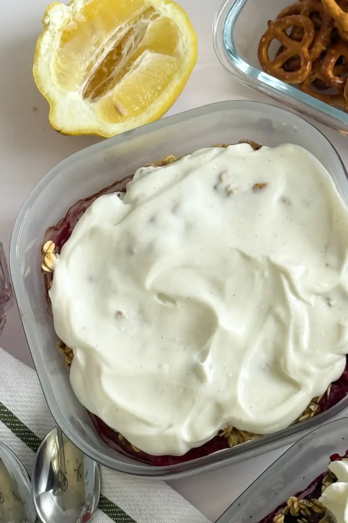 A close-up of the strwaberry cobbler with Greek yogurt spread across it in a glass container on a counte.