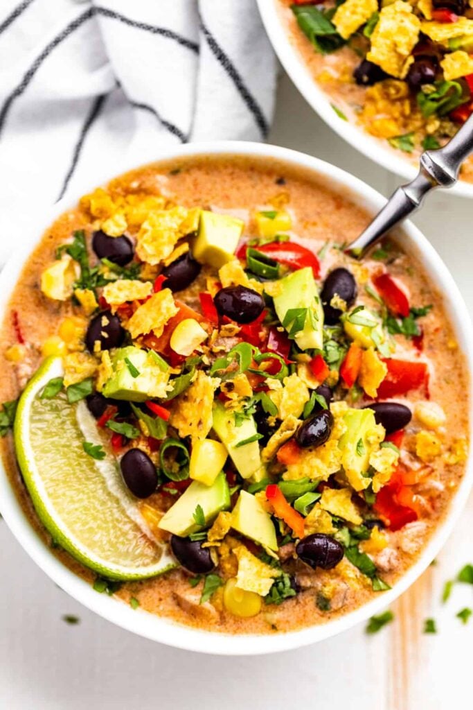 A birds-eye view of a bowl of creamy taco soup with a spoon in it on a table.