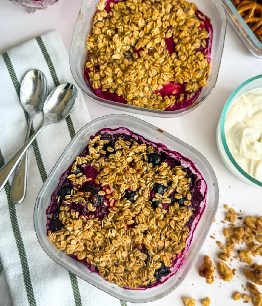 A birds-eye view of two fruit cobblers right ouf of the oven on a counter next to spoons and Greek yogurt.