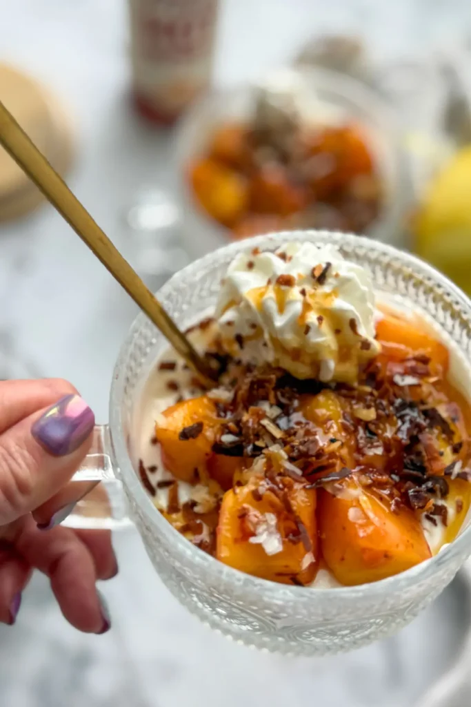 Someone holding the handle of a mango cheesecake bowl, fully assembled with a gold spoon in it. 