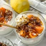 Beautifully assembled mango cheesecake bowls with toasted coconut, hot honey, and whipped cream on a counter next to lemon and a lemon zester.