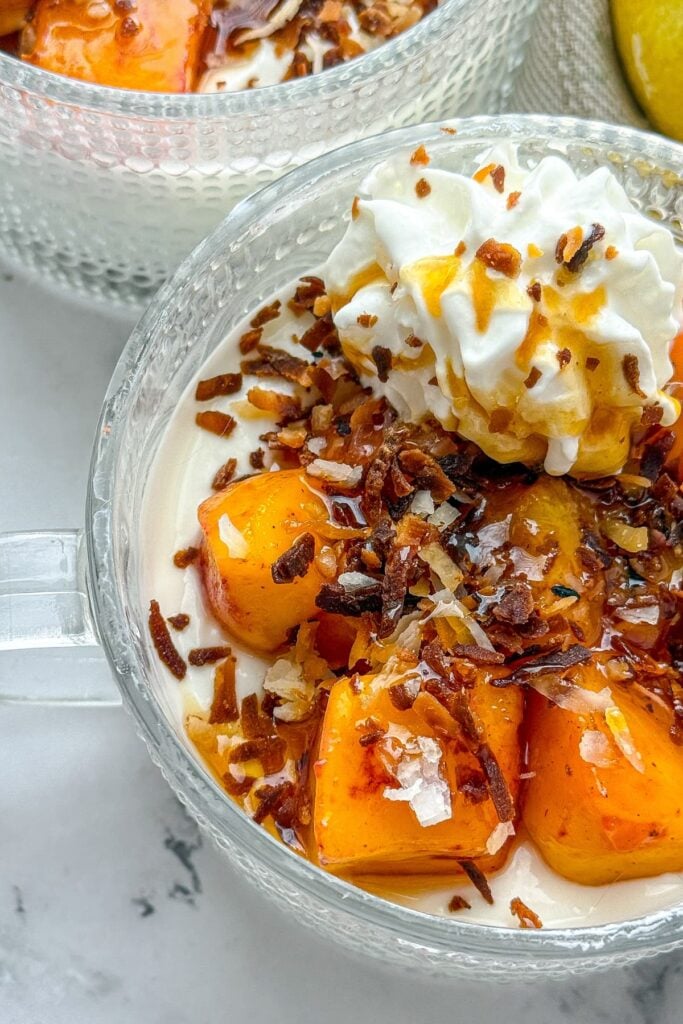 A close-up of a mango cheesecake bowl topped with whipped cream and toasted coconut on a counter.