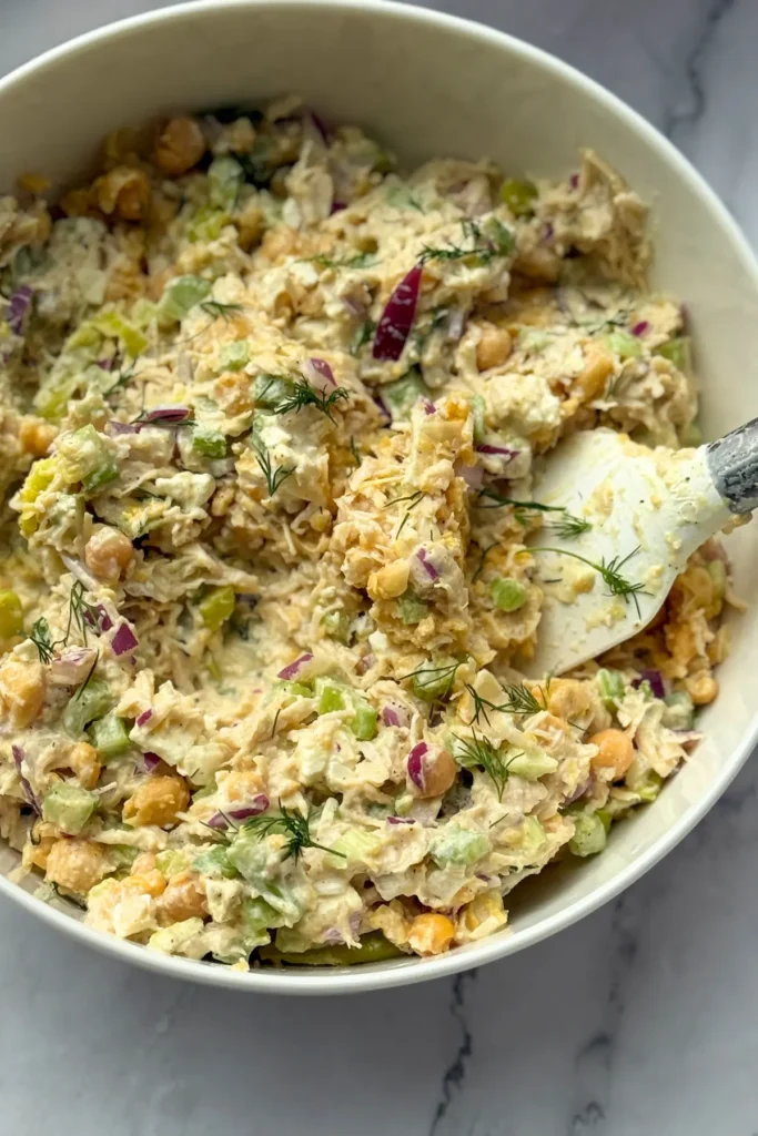 A birds-eye view of a large bowl of pepperoncini chicken salad with a spatula in it. 