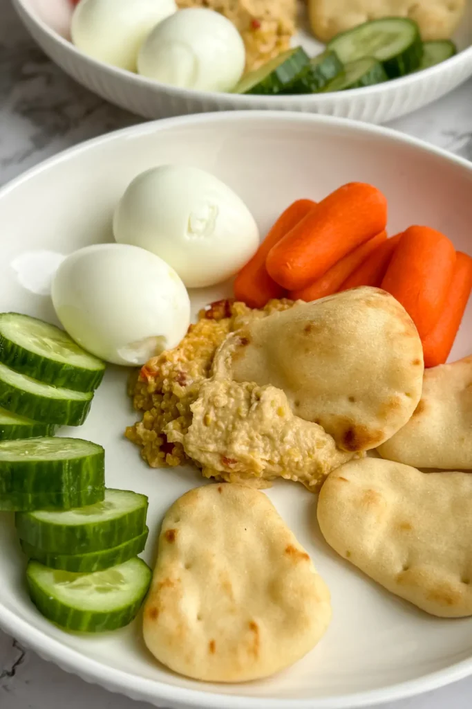 A snack plate with naan dippers, cucumbers, carrots, hard-boiled eggs and hummus.