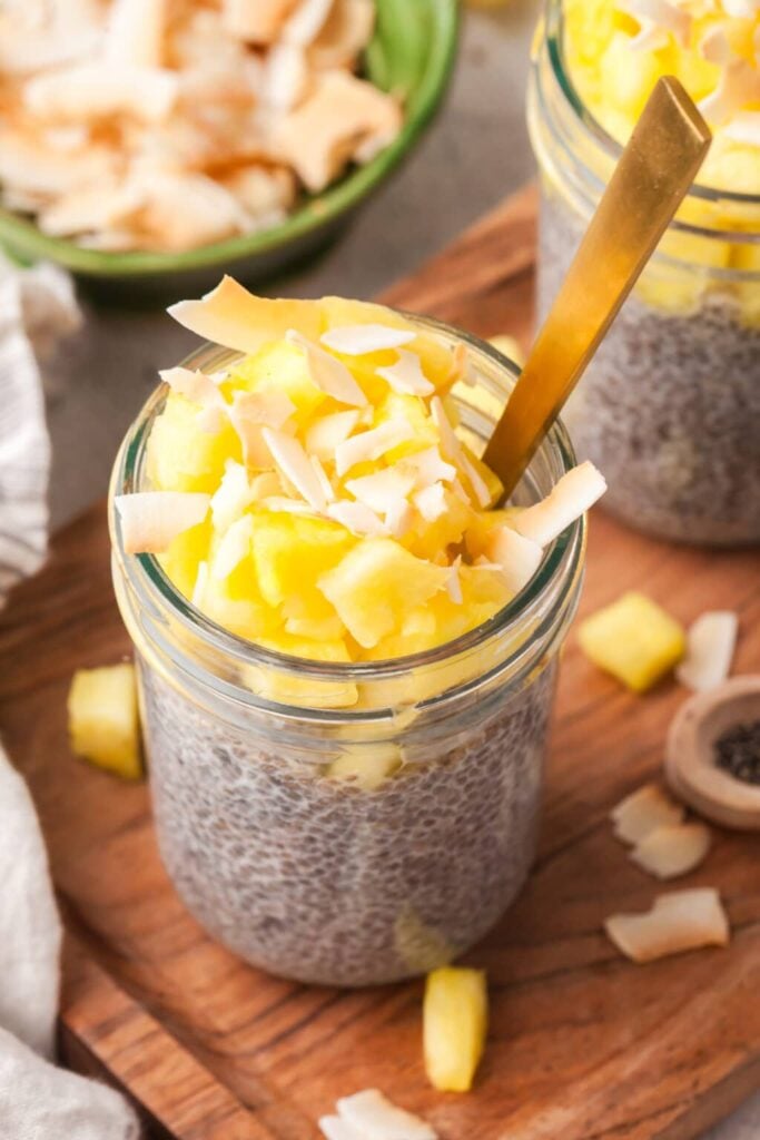 A birds-eye view of a tropical chia pudding in a glass topped with fresh pineapple with a spoon in it on a wooden cutting board.
