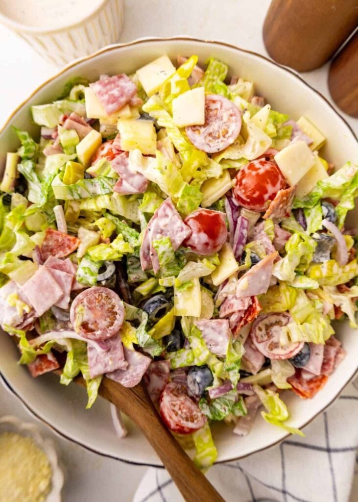 A birds-eye view of a grinder salad with a wooden spoon in it on a table.