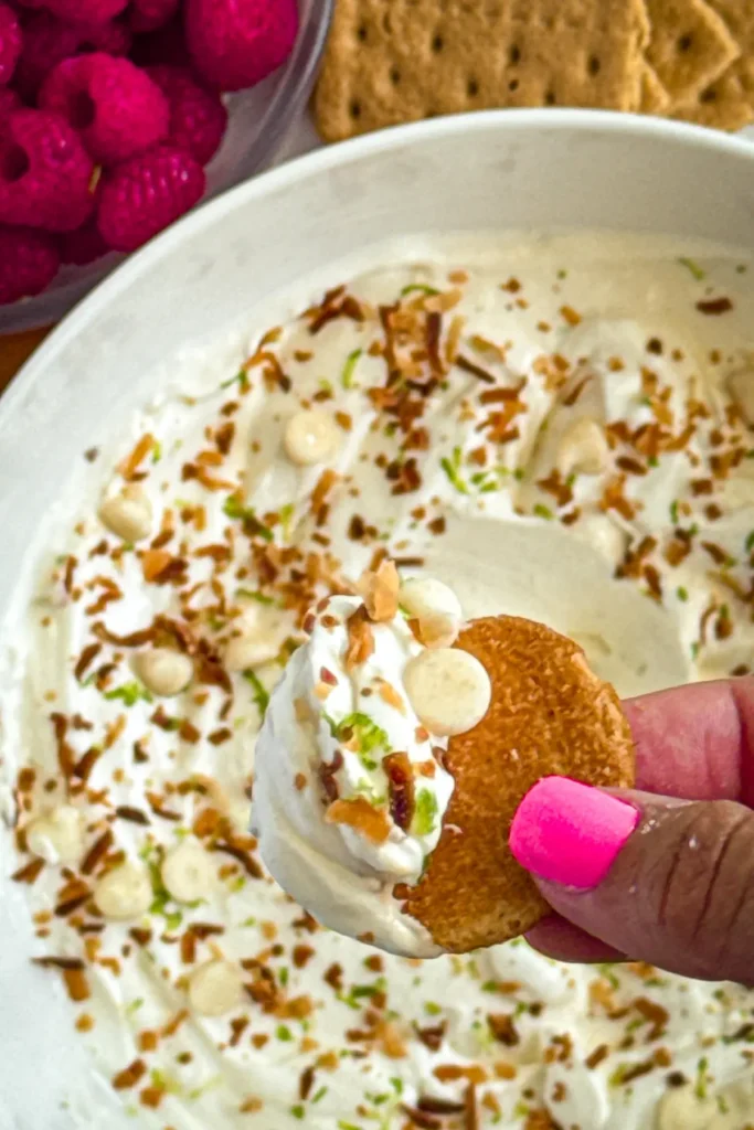 A vanilla wafer after being dipped in the key lime pie dip over a large bowl.