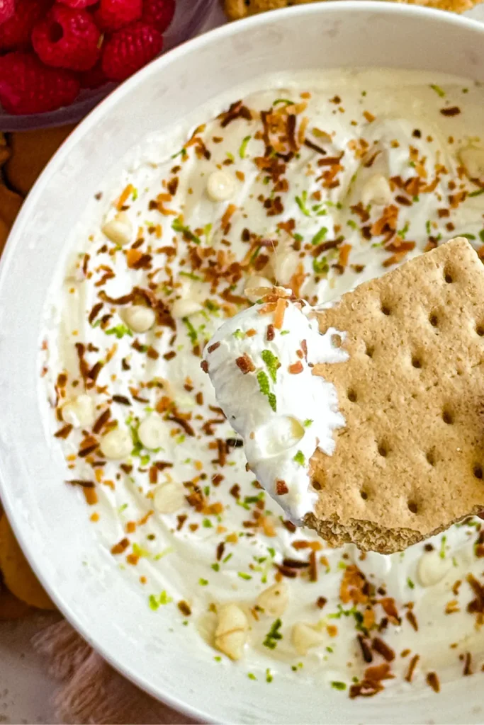 A close-up of a graham cracker with key lime pie dip on it over a big bowl of dip.