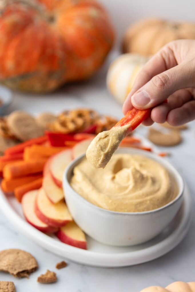 Someone dipping fruit into a bowl of pumpkin dip on a platter on a table. 