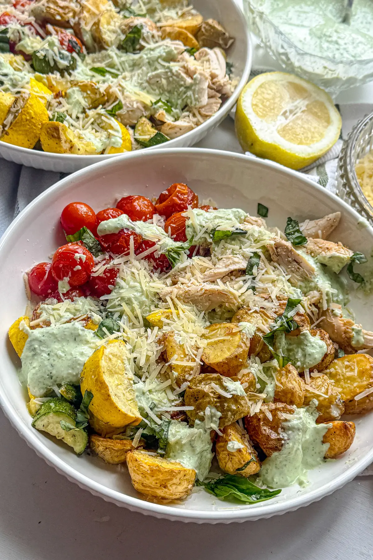 Two fully assembled parmesan basil chicken bowls on a table next to lemon wedges.