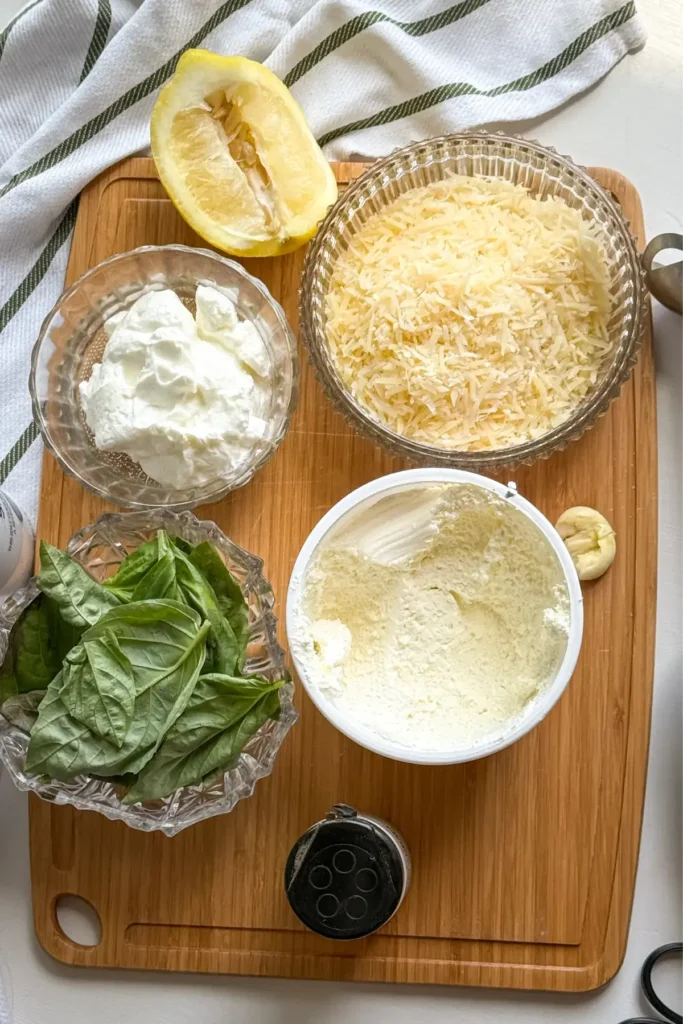 The ingredients for the basil and parmesan sauce on a wooden cutting boardon a counter.