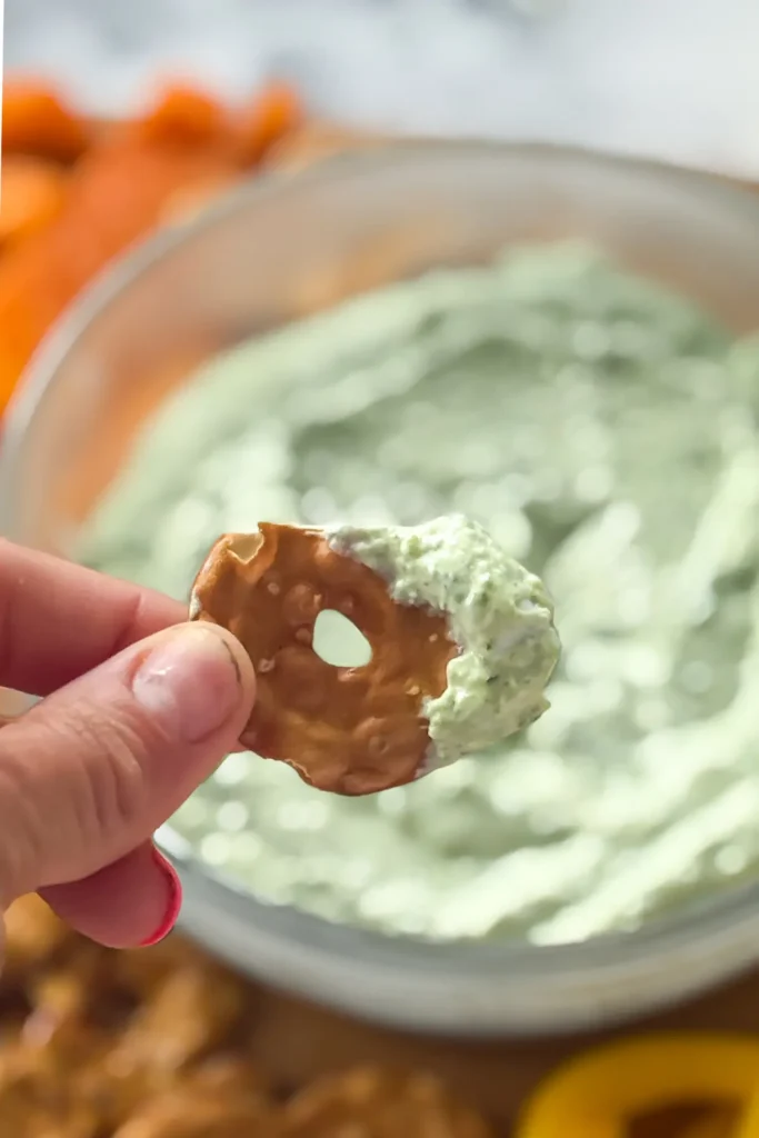 A close-up of the parmesan basil dip on a pretzel crisp, being held up in someone's hand.