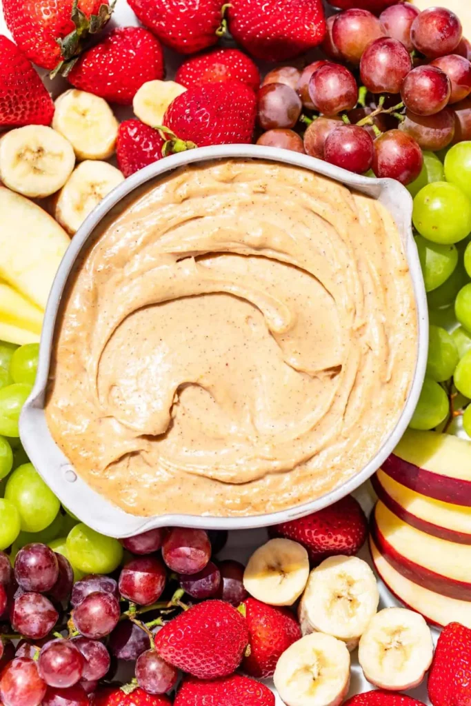 A large bowl of peanut butter dip surrounced by fresh fruit.